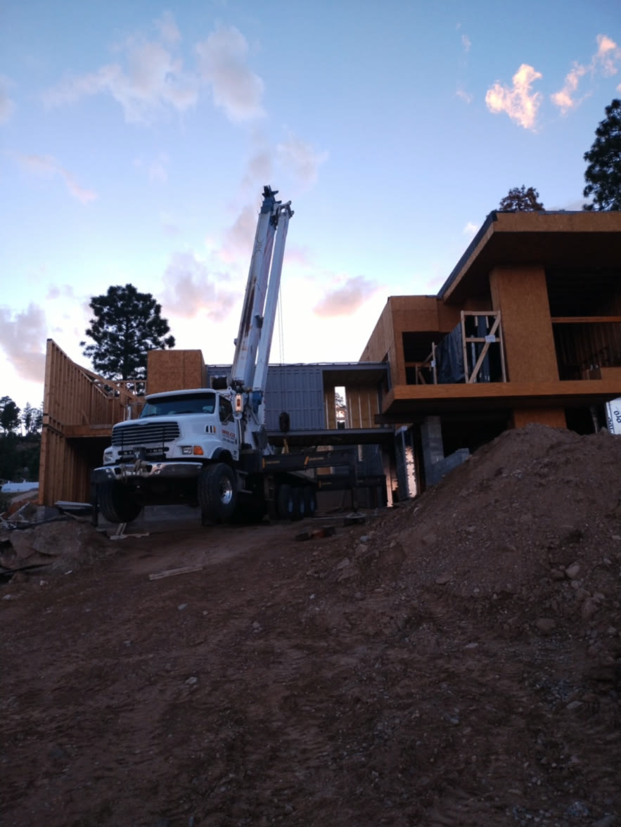 Crane setting the steel bridge between two framed wings of a custom home at dusk, built by Infinity Builders in New Mexico