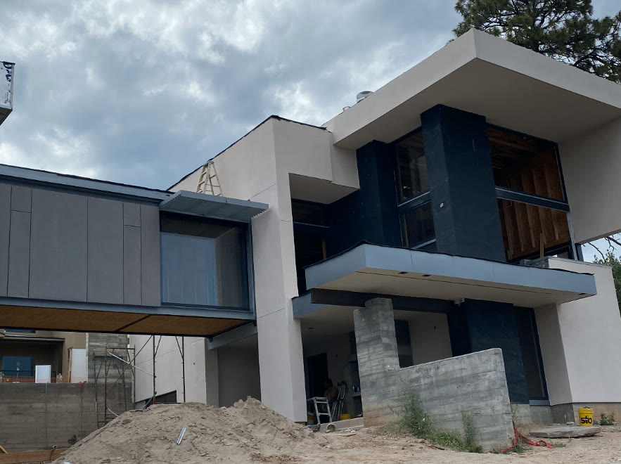 Modern custom home with stucco walls, dark accents, and a cantilevered glass bridge room, built by Infinity Builders in New Mexico
