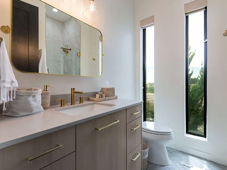 Oak vanity with brushed brass fixtures and tall desert-view windows in a Corrales, NM custom home by Infinity Builders