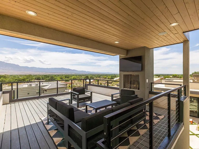 Covered rooftop deck with cable railing and Sandia Mountain views at a Corrales, NM custom home by Infinity Builders