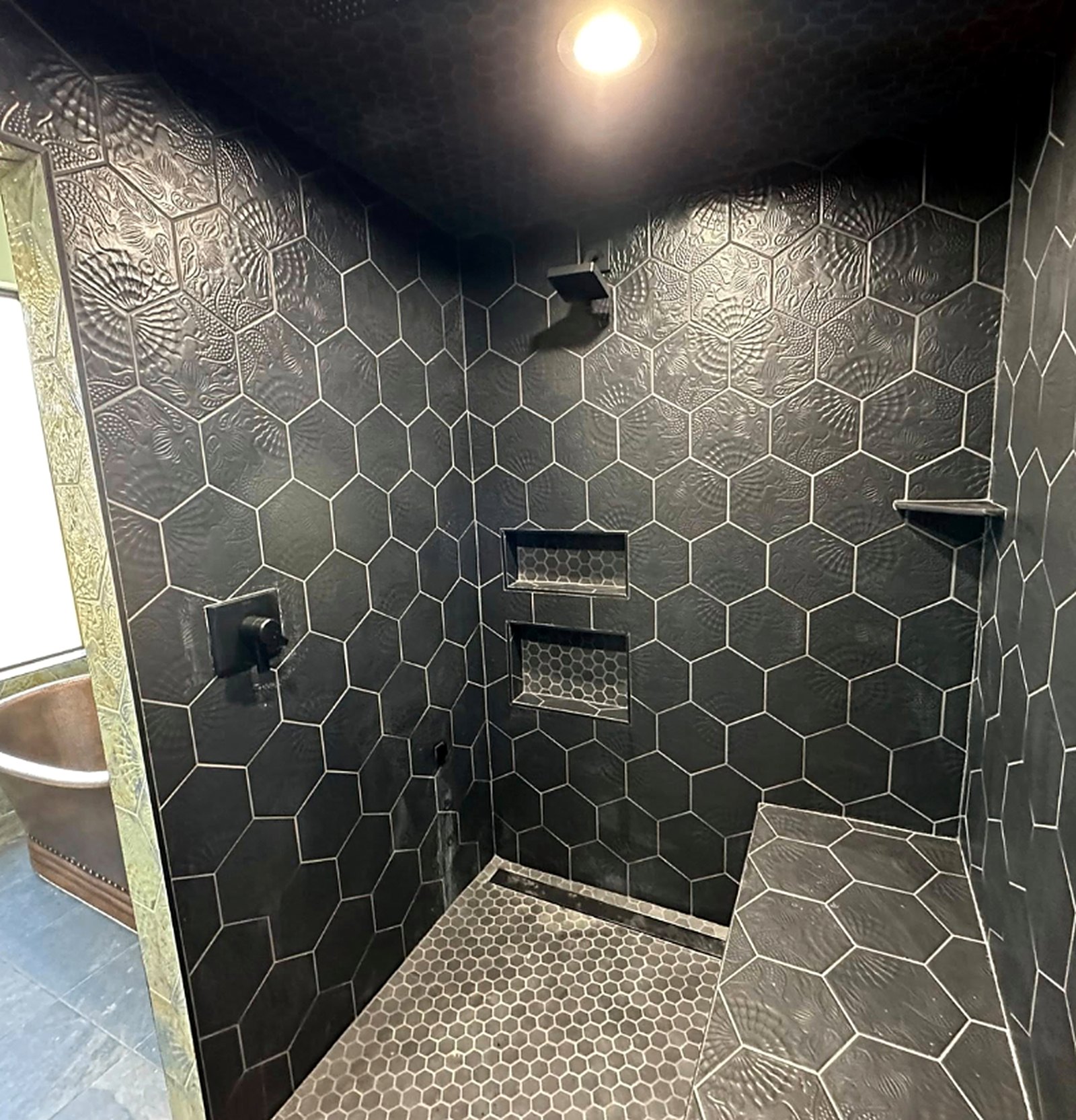 Walk-in shower with charcoal hexagon tile, niches, and bench