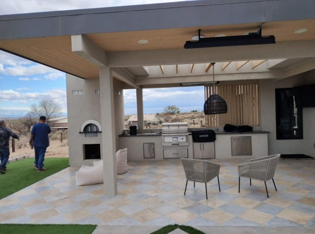 Covered outdoor kitchen with built-in grill, pizza oven, and tiled patio, built by Infinity Builders in New Mexico
