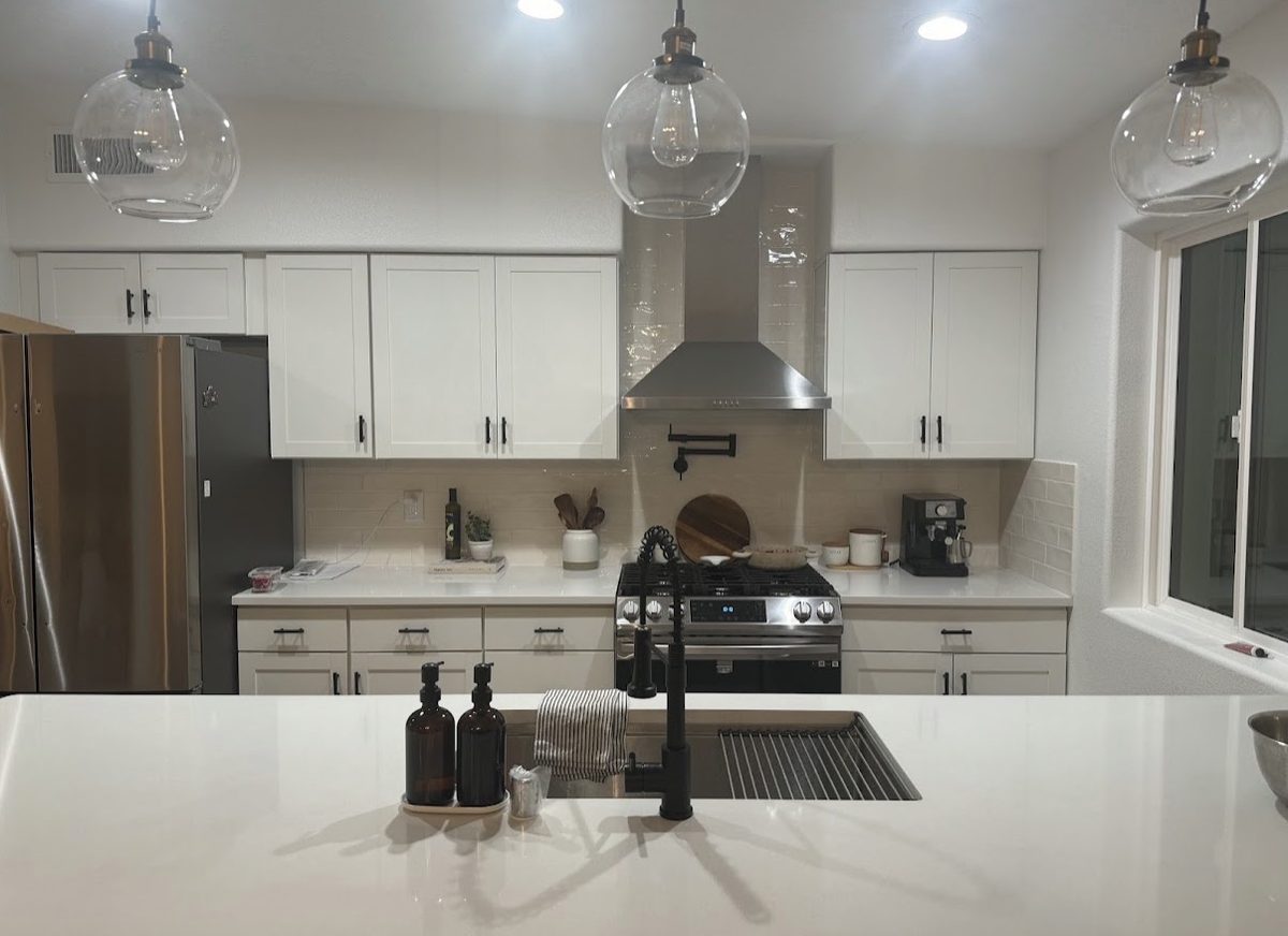 White shaker kitchen with quartz island, glass pendant lights, and matte black fixtures, built by Infinity Builders in New Mexico