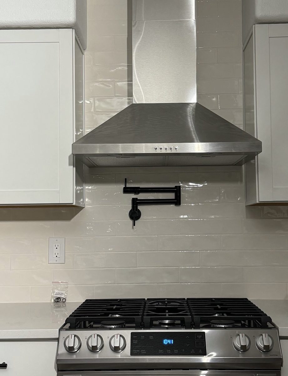 Glass subway tile backsplash with matte black pot filler and stainless range hood, built by Infinity Builders in New Mexico